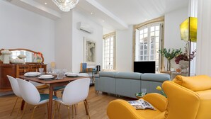 En moderne stue med sofa, gul lænestol, spisebord med stole og et fjernsyn.