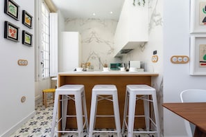 Une cuisine moderne avec un dosseret en marbre, des tabourets de bar blancs et un plan de travail en bois.