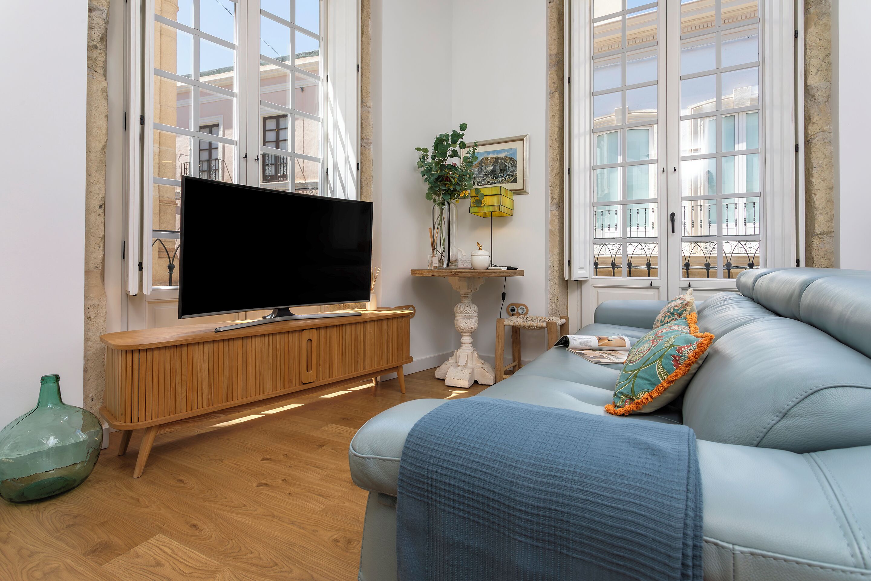 Uma sala de estar com televisão, sofá, console de madeira e uma grande janela com vista.