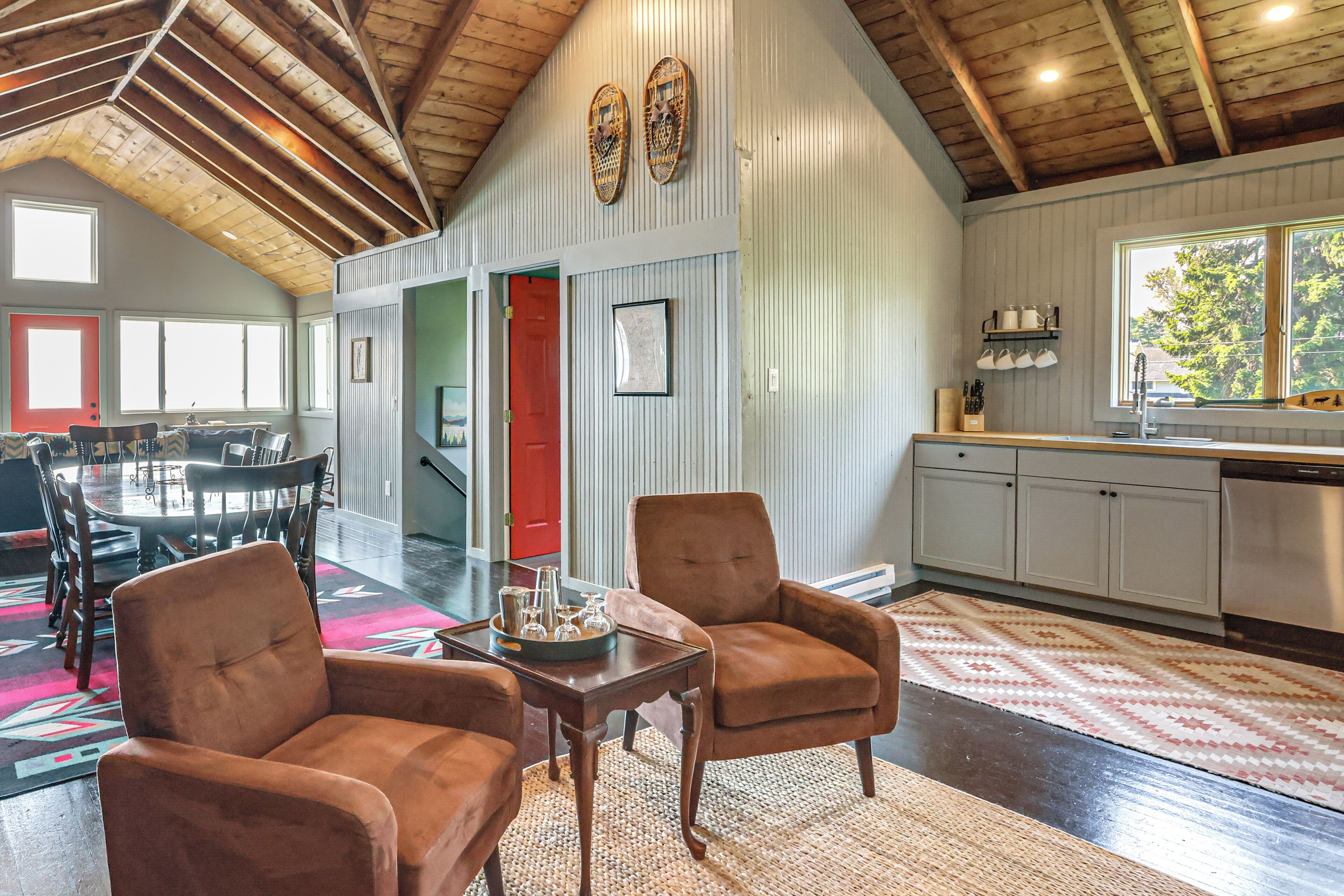 A spacious living area with a high ceiling, a dining area, and a kitchen with a large window.