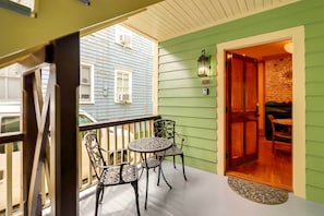 Un balcon avec une table et des chaises, une porte donnant sur l’intérieur et une vue sur la maison voisine.
