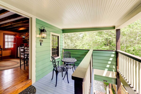 A covered porch with a green exterior, wooden flooring, and a seating area with two chairs and a table.