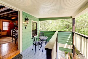 Une véranda couverte aux murs verts, avec un plancher en bois et une table entourée de chaises.