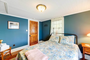 Une chambre à coucher avec un lit, une porte en bois, un tableau encadré au mur et une fenêtre avec des rideaux.