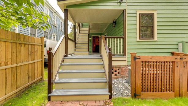 Eine Holztreppe führt zu einem grünen Haus mit einer Veranda, einem Holzzaun und einem Ziegelweg.