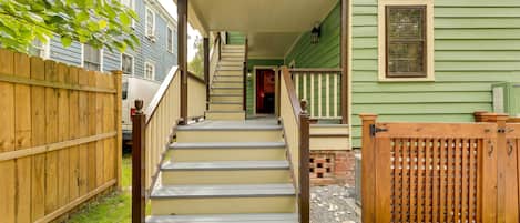 Eine Holztreppe führt zu einem grünen Haus mit einer Veranda, einem Holzzaun und einem Ziegelweg.