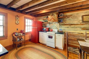 A kitchen with wooden beams, a red refrigerator, a white stove, and a herringbone-patterned backsplash. - Twin Victorian Apts in Downtown New Bern (New Bern)