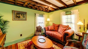 Ein gemütliches Wohnzimmer mit Holzboden, einem gemusterten Sofa, einem runden Couchtisch und einem gerahmten Bild an der Wand.