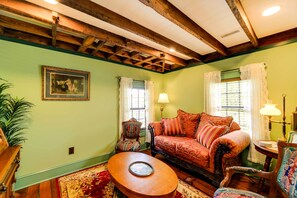 A cozy living room with a wooden ceiling, a patterned sofa, a round coffee table, and a framed picture on the wall. - Twin Victorian Apts in Downtown New Bern (New Bern)