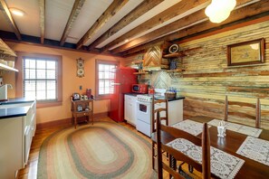 Una cocina con vigas de madera, un refrigerador rojo, una estufa y una mesa de comedor con sillas.