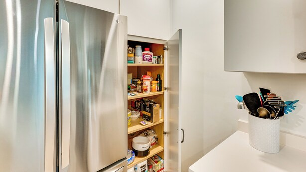 Une cuisine moderne dotée d’un réfrigérateur en acier inoxydable, d’étagères ouvertes remplies de divers produits alimentaires et d’un plan de travail sur lequel se trouvent une machine à café et des ustensiles.