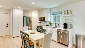 Une cuisine moderne avec des meubles blancs, des appareils en acier inoxydable et un coin repas comprenant une table et des chaises.