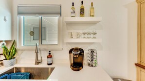 Une cuisine moderne dotée d’un évier encastré, d’une machine à café et de bouteilles de vin disposées sur une étagère.