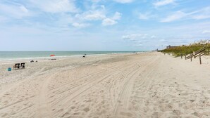 Une vaste plage de sable fin, un ciel dégagé, quelques parasols et une clôture en bois qui longe le rivage.