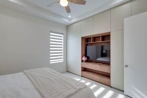 Ein Schlafzimmer mit Bett, Kleiderschrank, Deckenventilator und einem Fenster mit Jalousien.