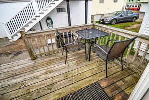A wooden deck with a metal table and chairs, a wooden railing, and a staircase leading to an upper level.