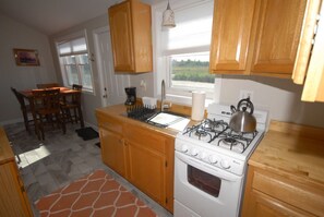 A compact kitchen with wooden cabinets, a gas stove, a built-in oven, and a dining area with a table and chairs.