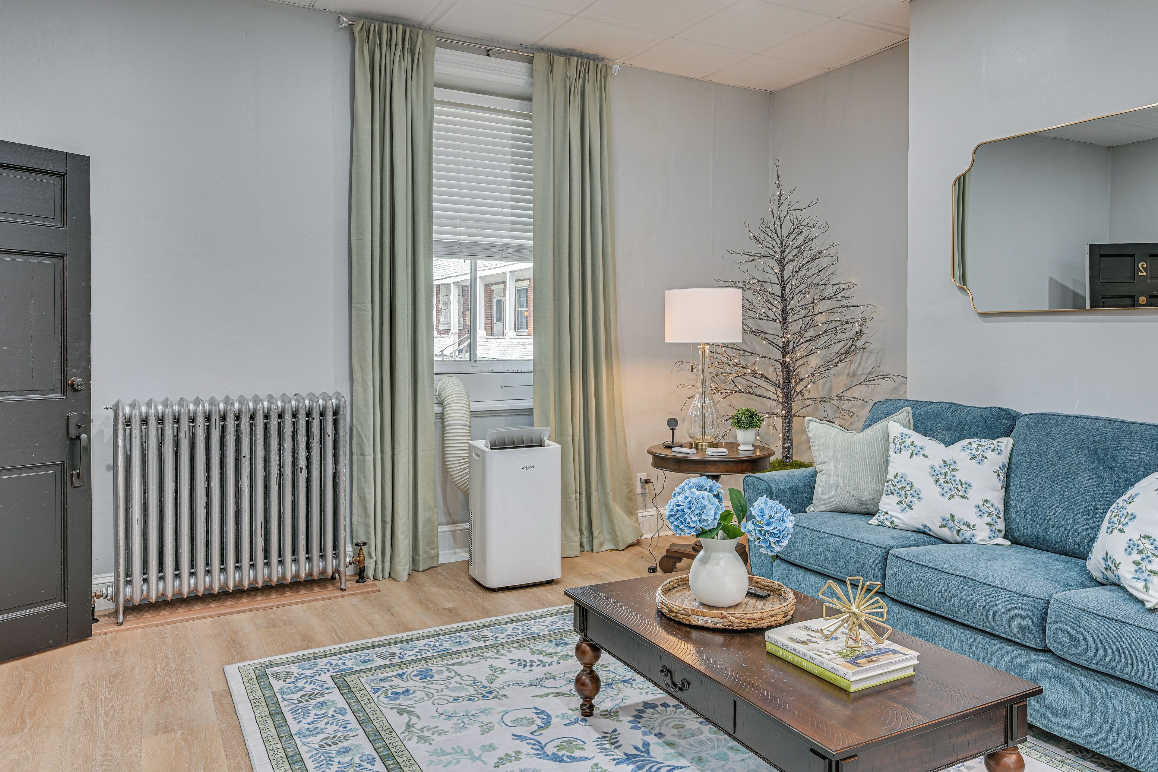 A living room with a blue sofa, a radiator, a white air conditioner, and a decorative tree.