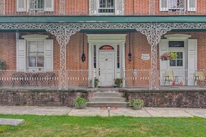 A brick building with a white door and windows, a green awning, and a sign that reads 'McCausland Mansion.'