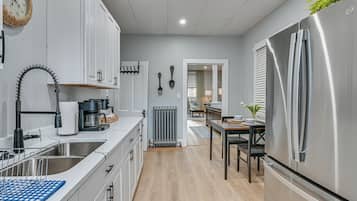 A modern kitchen with white cabinetry, a stainless steel refrigerator, and a coffee machine.