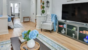 A living room with a television, a chair, a coffee table with a vase and flowers, and a bookshelf.