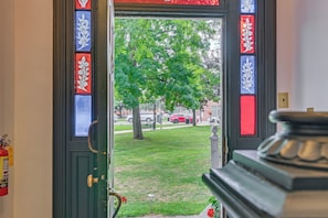 A door with stained glass panels, a fire extinguisher, and a view of a green lawn and trees.