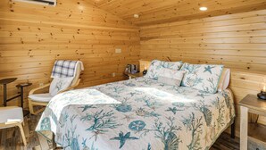 Een slaapkamer in een houten chalet, met een bed, een stoel, een klein tafeltje en een airconditioner.