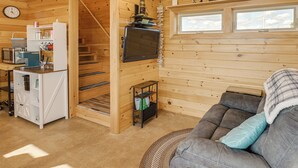 Een gezellig cabin interieur met een keukenhoek, een zithoek met een bank, een aan de muur bevestigde televisie en een houten trap.