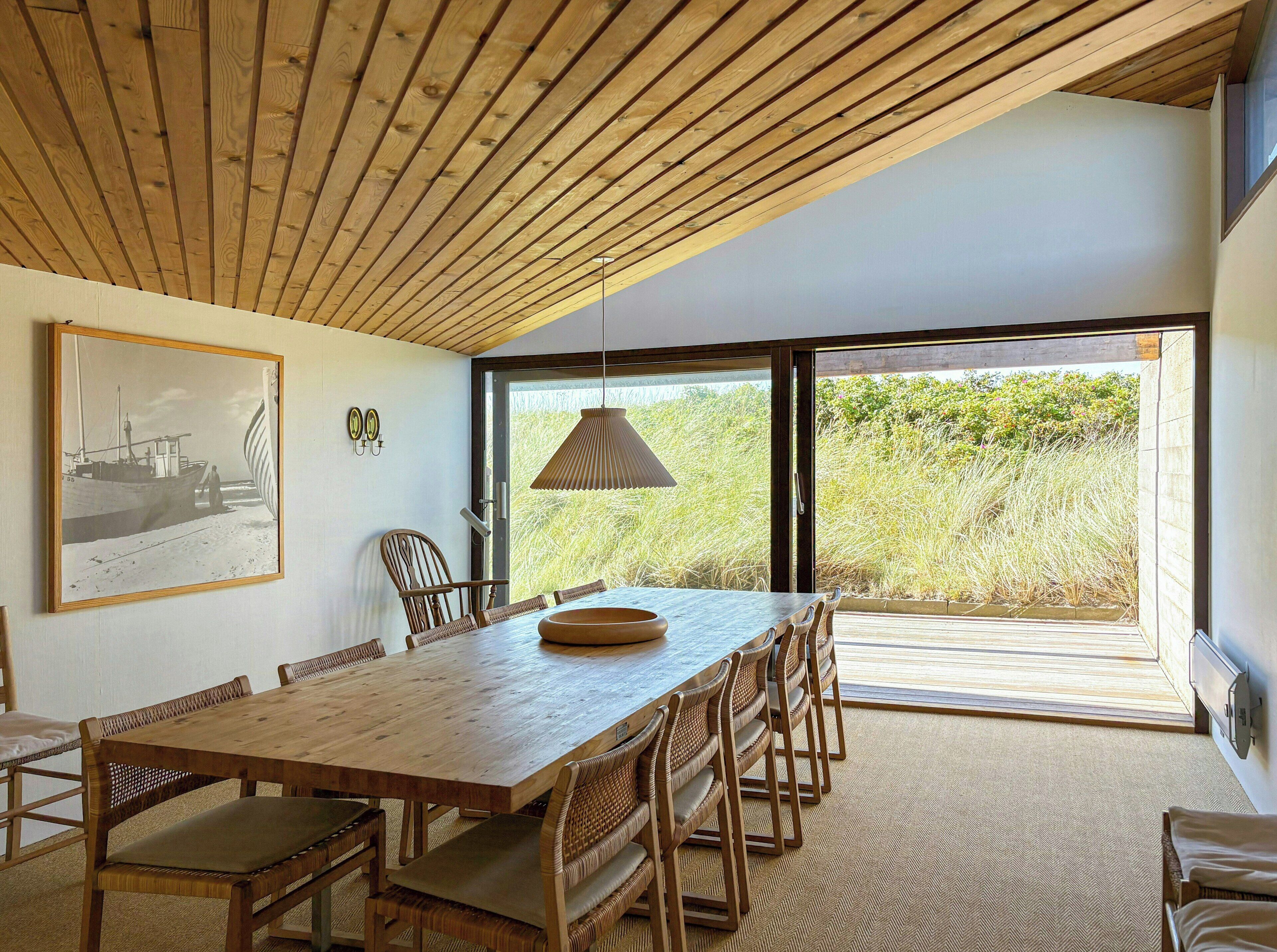 Un comedor con una mesa y sillas de madera, una lámpara colgante y un cuadro en la pared.