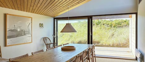 Un coin repas avec une table et des chaises en bois, un luminaire suspendu et un tableau encadré au mur.