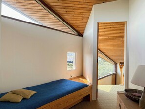 Une petite chambre avec un lit simple, un plafond en bois et une fenêtre.