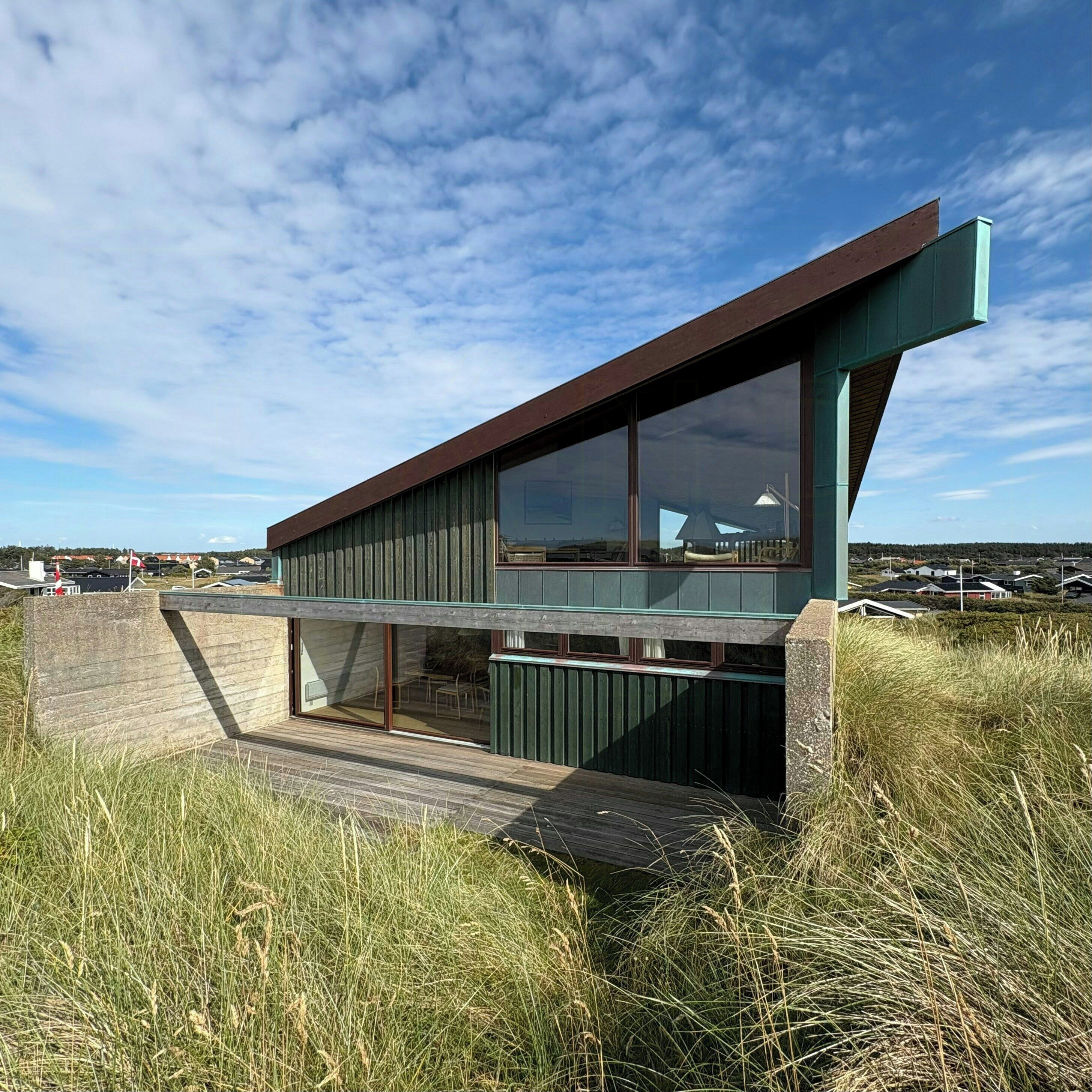 A modern house with a sloped roof, large windows, and a wooden deck.
