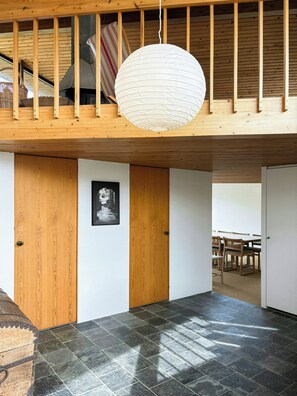 A room with a wooden ceiling, a hanging light fixture, a black and white photograph on the wall, and a dining area in the background. - Architect-designed holiday home close to the beach (Løkken)