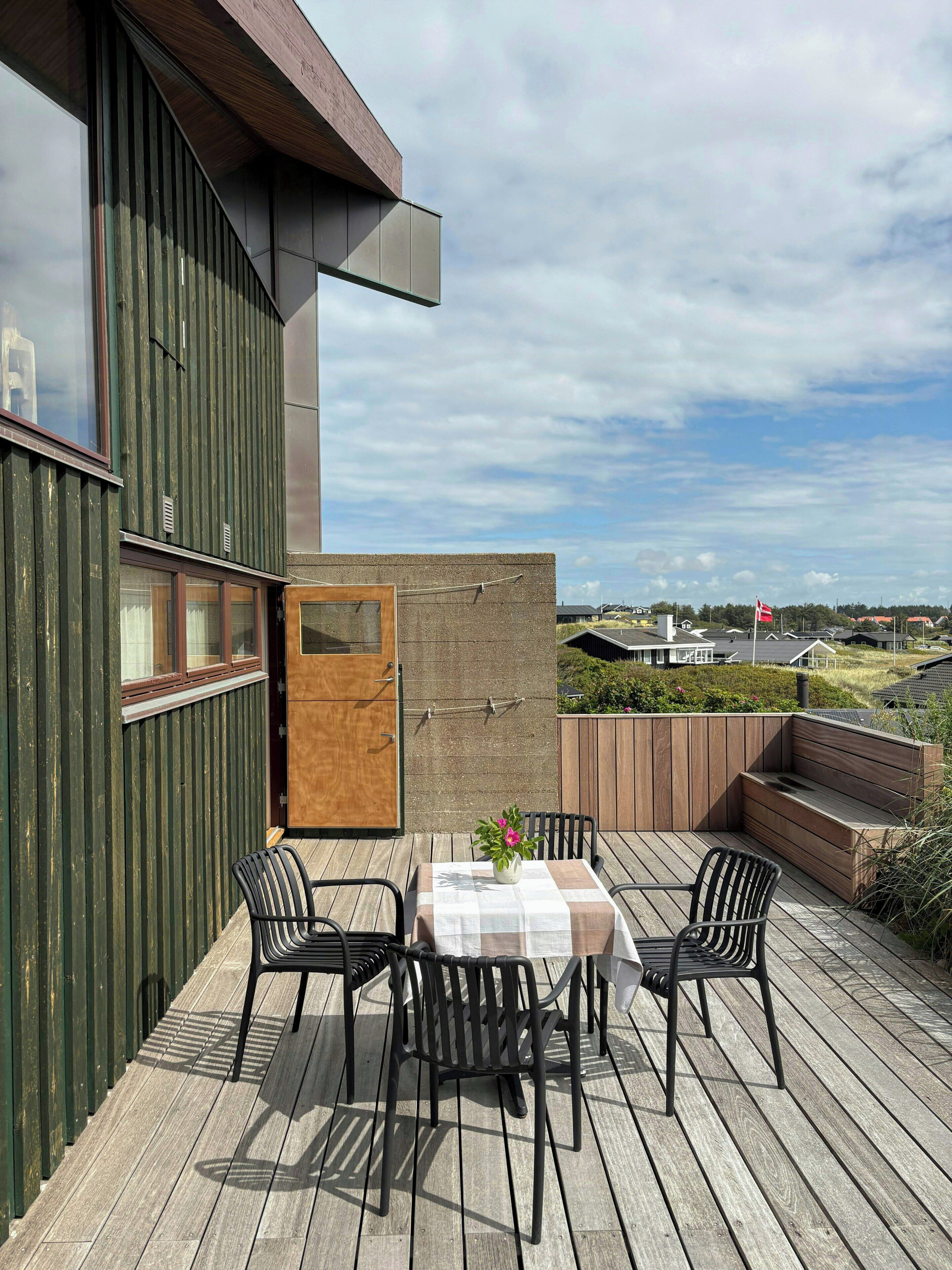 Un espacio exterior moderno con una mesa y sillas, una terraza de madera y vistas del paisaje circundante.