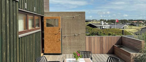 Un espacio exterior moderno con una mesa y sillas, una terraza de madera y vistas del paisaje circundante.