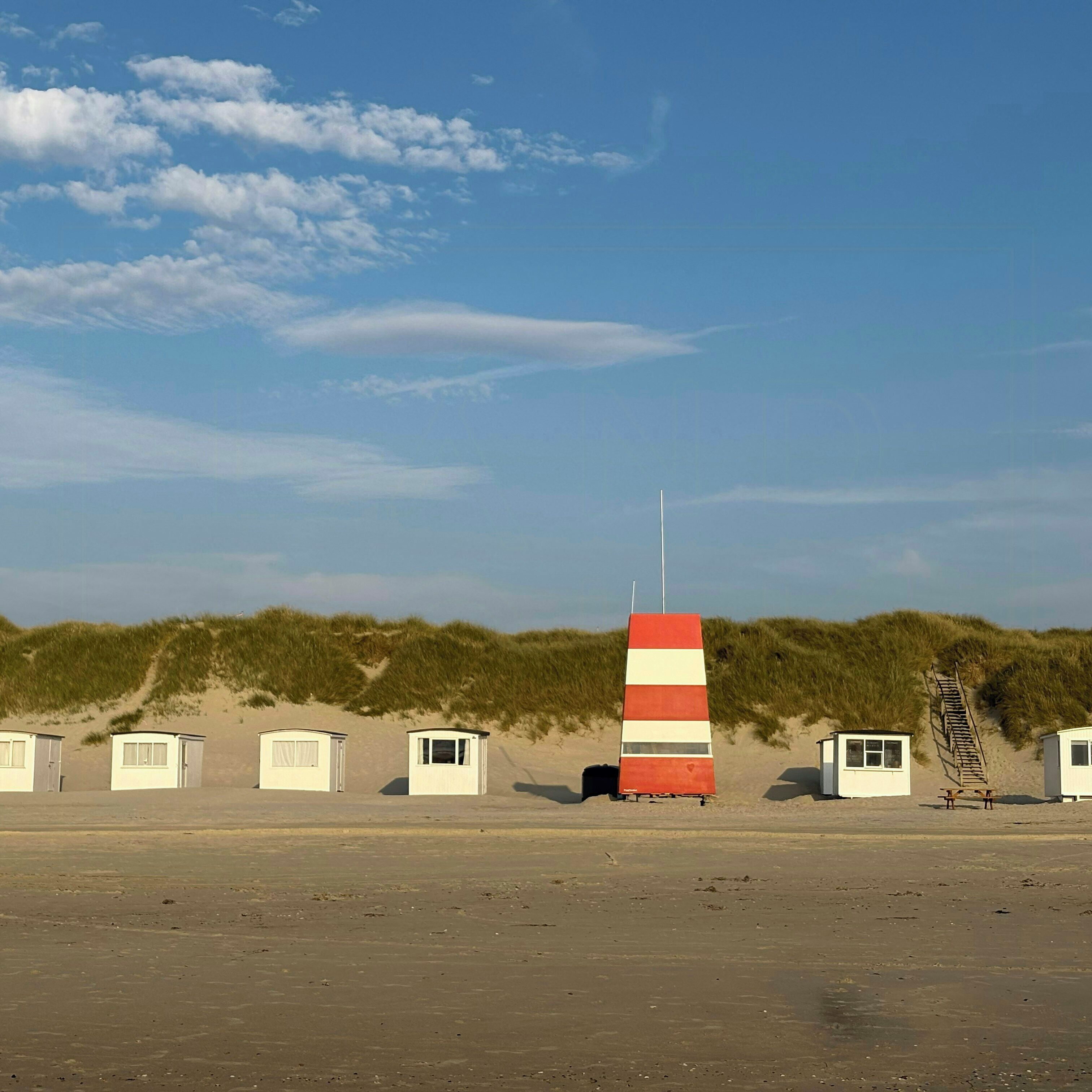 Ein Strand mit Dünenhütten, einem Rettungsturm und einer Sandburg.