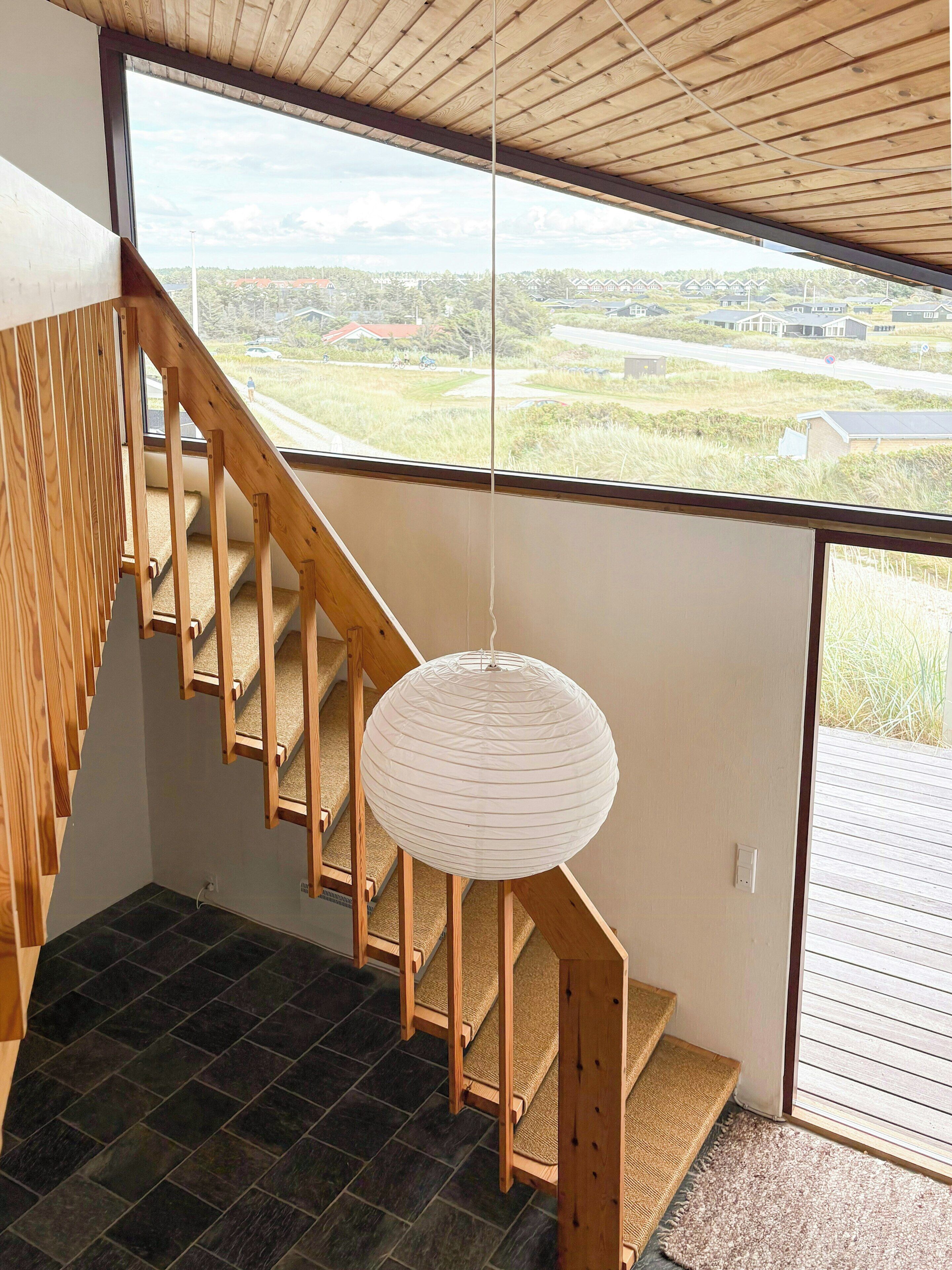 Eine Holztreppe mit Blick auf eine Landschaft durch ein großes Fenster.