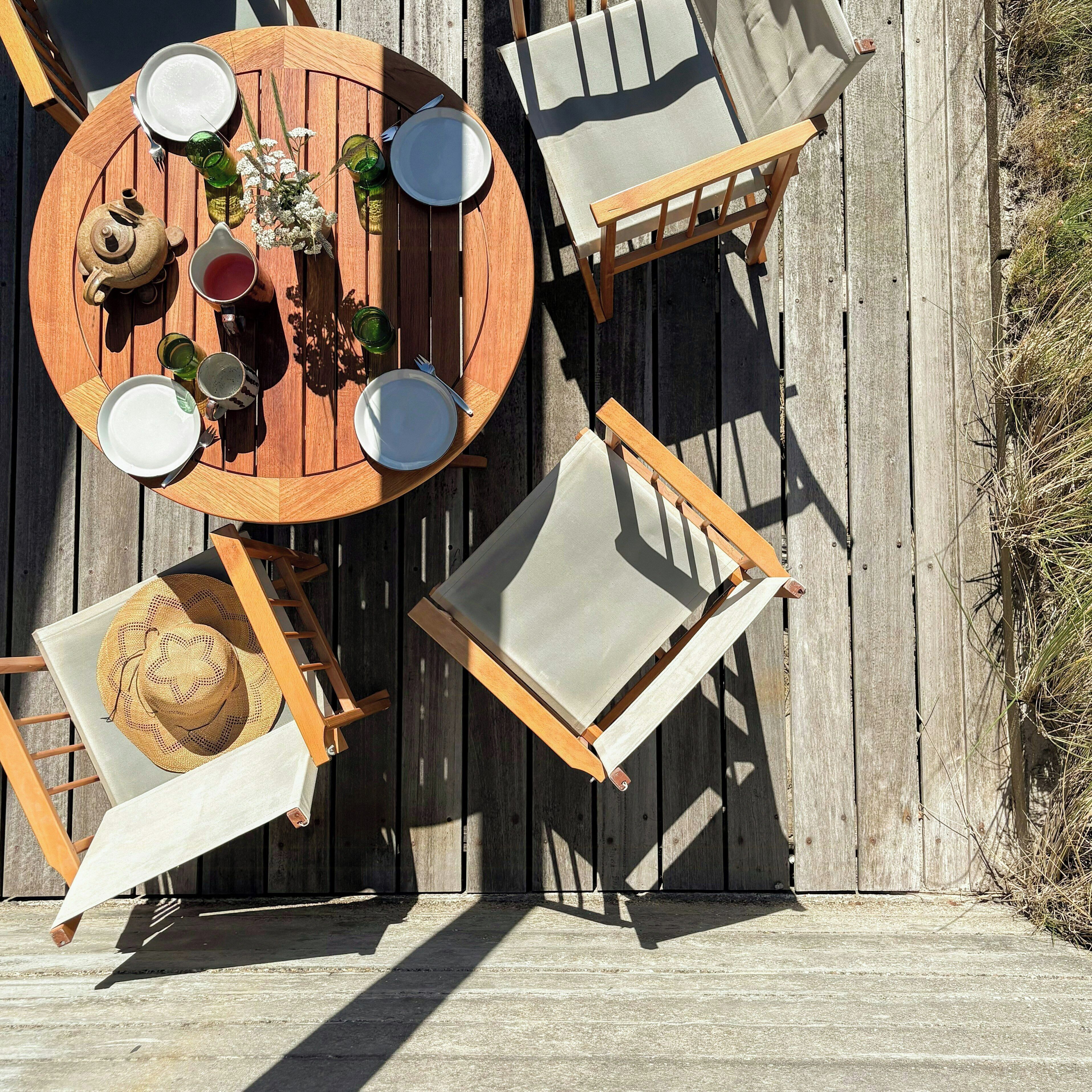 A wooden deck with a round table, four chairs, and a dining set including plates, cups, and a teapot.