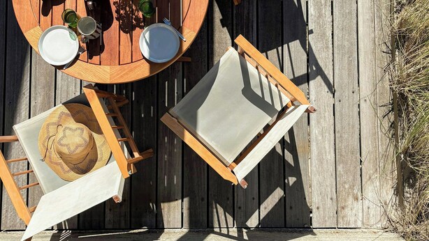 A wooden deck with a round table, four chairs, and a dining set including plates, cups, and a teapot. - Architect-designed holiday home close to the beach (Løkken)
