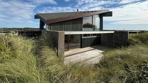 A modern house with a flat roof, large windows, and a wooden deck. - Architect-designed holiday home close to the beach (Løkken)