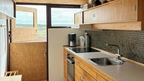 A compact kitchen with wooden cabinets, a built-in oven, a sink, and a window offering a view. - Architect-designed holiday home close to the beach (Løkken)
