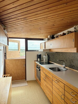 Eine kleine Küche mit Holzausstattung, einem Backofen, einem Spülbecken und einem Fenster mit Blick.