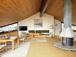 Un intérieur chaleureux avec un plafond en bois, une cheminée, un téléviseur et un coin repas comprenant des chaises et une table.