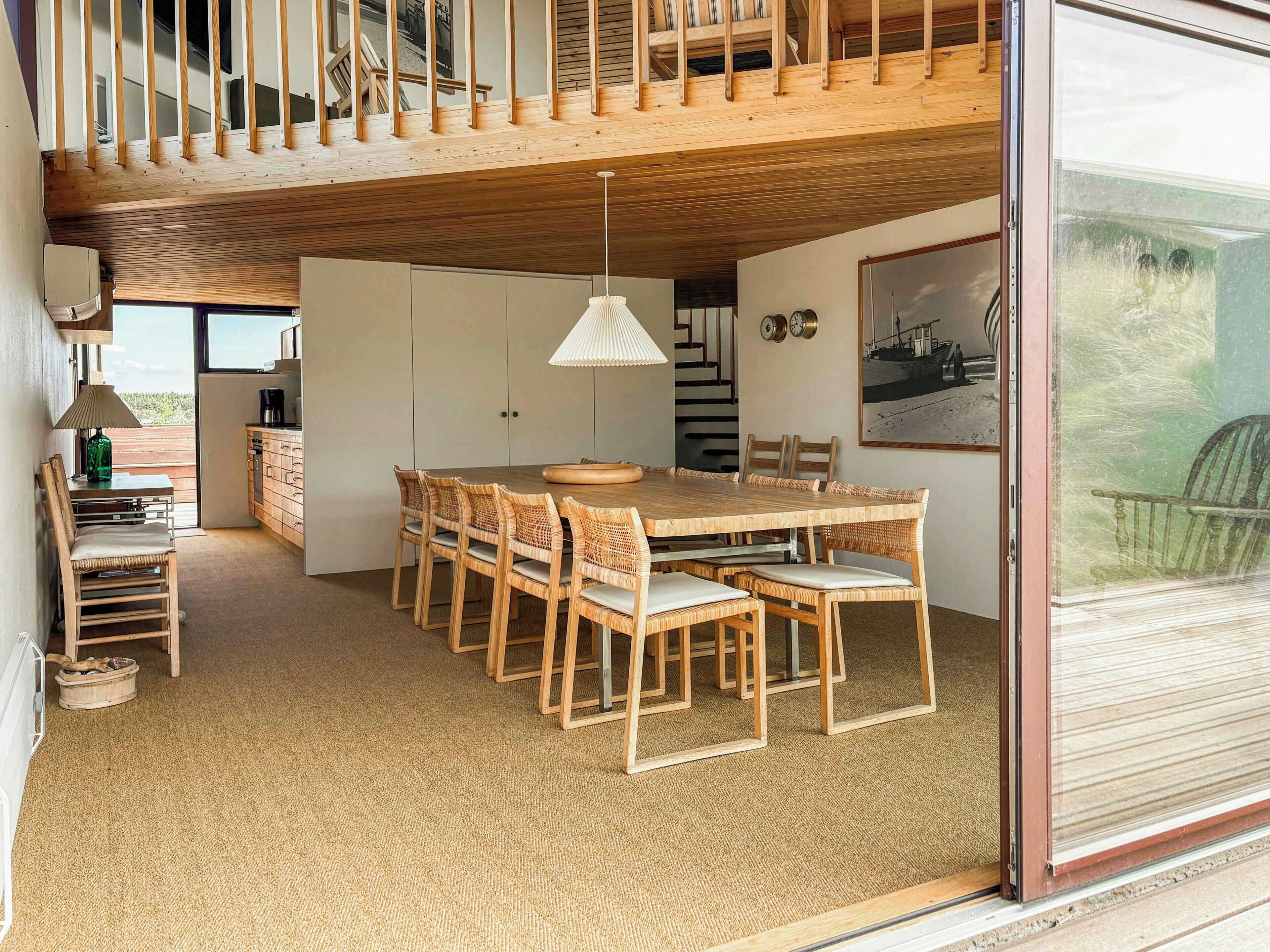 Comedor con mesa y sillas de madera, una lámpara colgante y vistas a través de un ventanal.