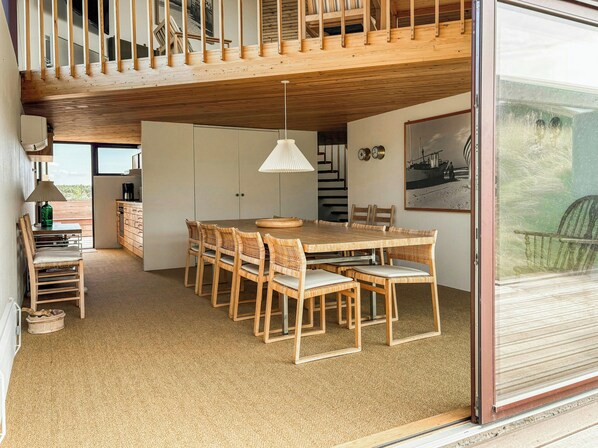 Un coin repas avec une table et des chaises en bois, une lampe suspendue et une vue à travers une porte vitrée.