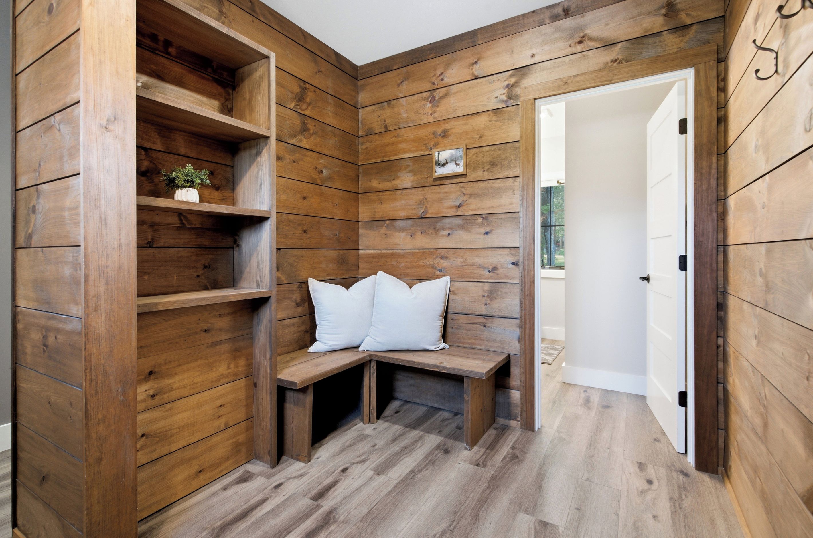 A wooden interior with a bench, shelves, and a door leading to another room.