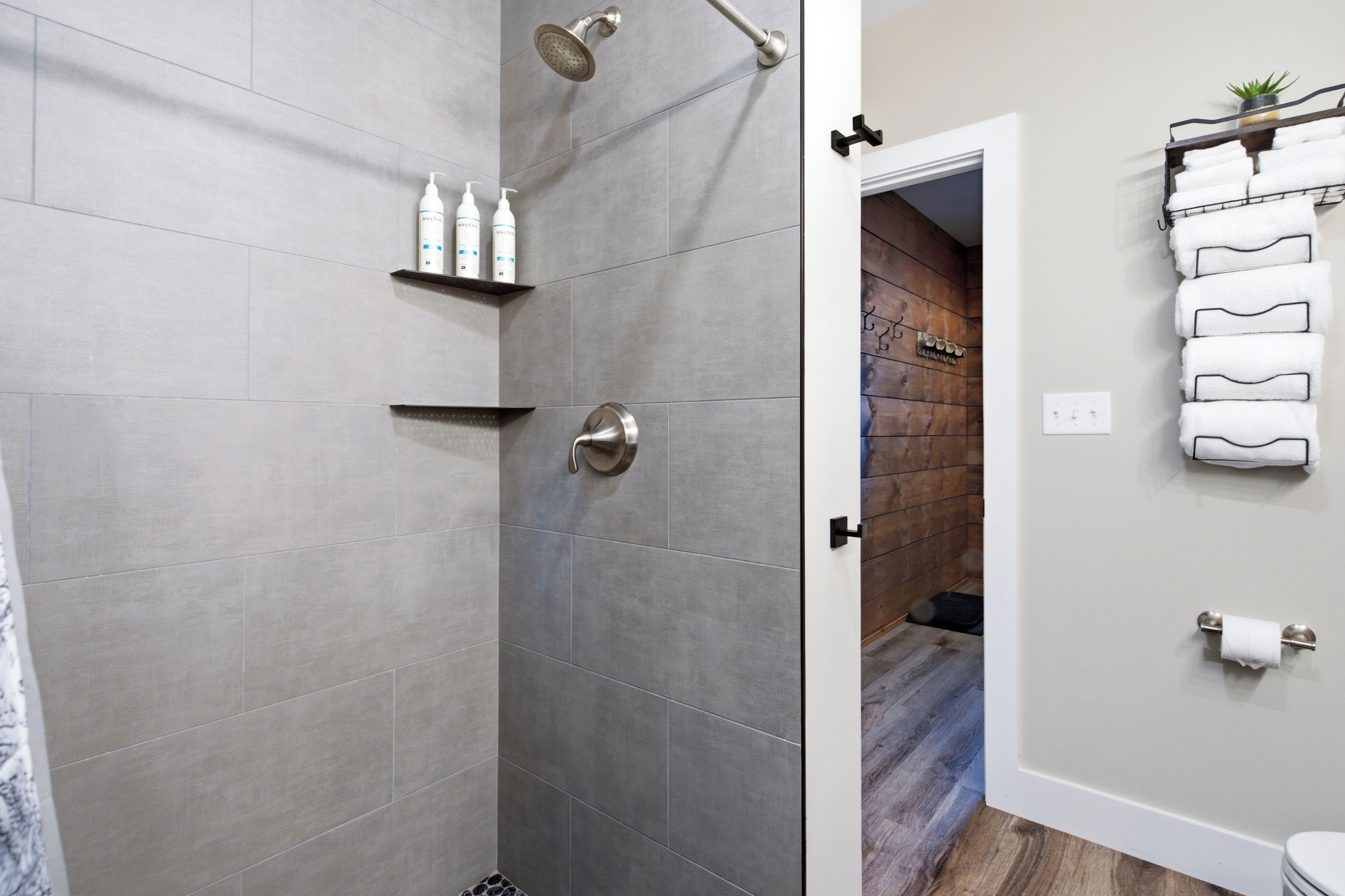 A modern bathroom with grey tiles, a shower, a toilet, and a towel rack with neatly folded towels.