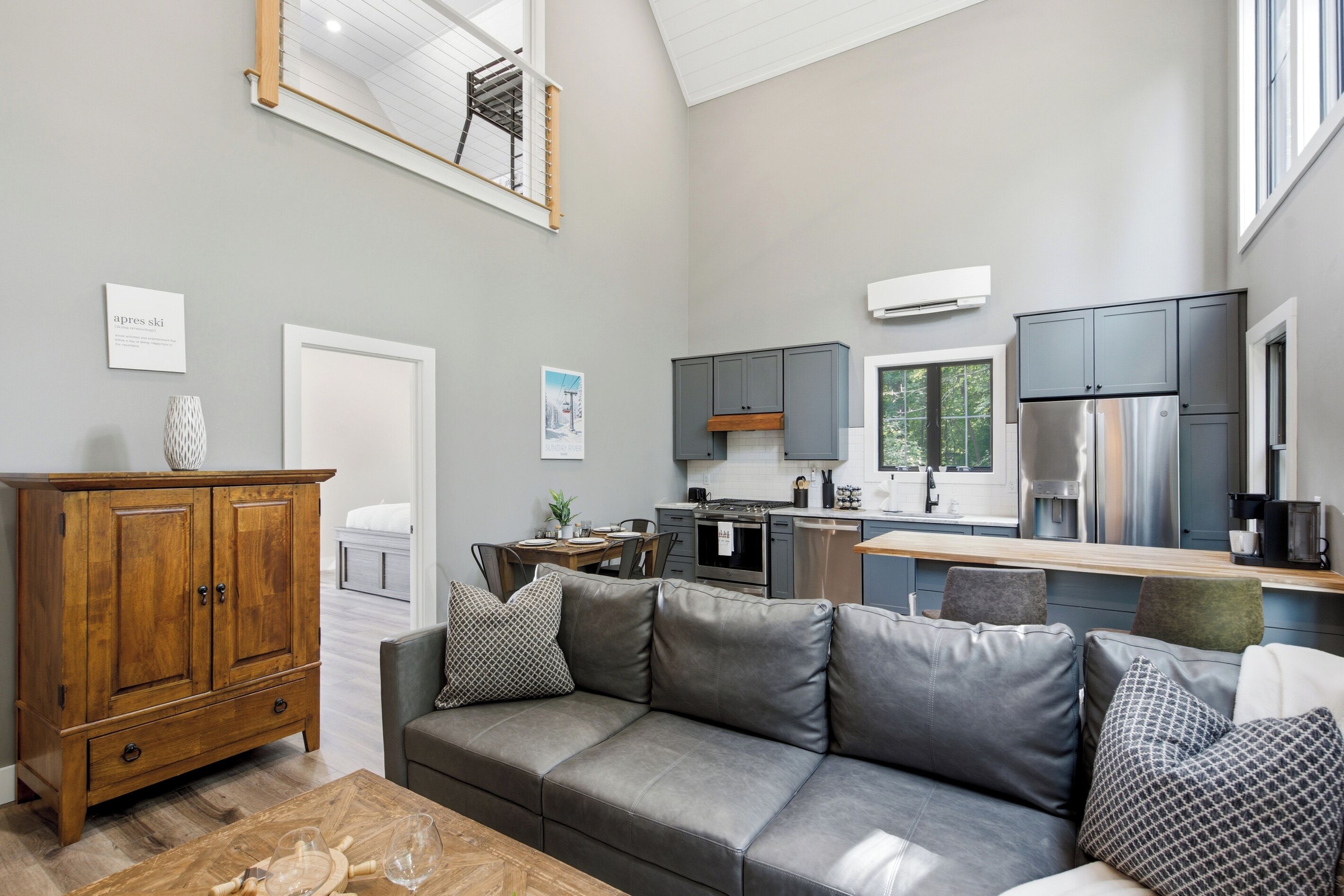 A modern kitchen with grey cabinets, a stainless steel refrigerator, and a dining area with a wooden table and grey sofa.