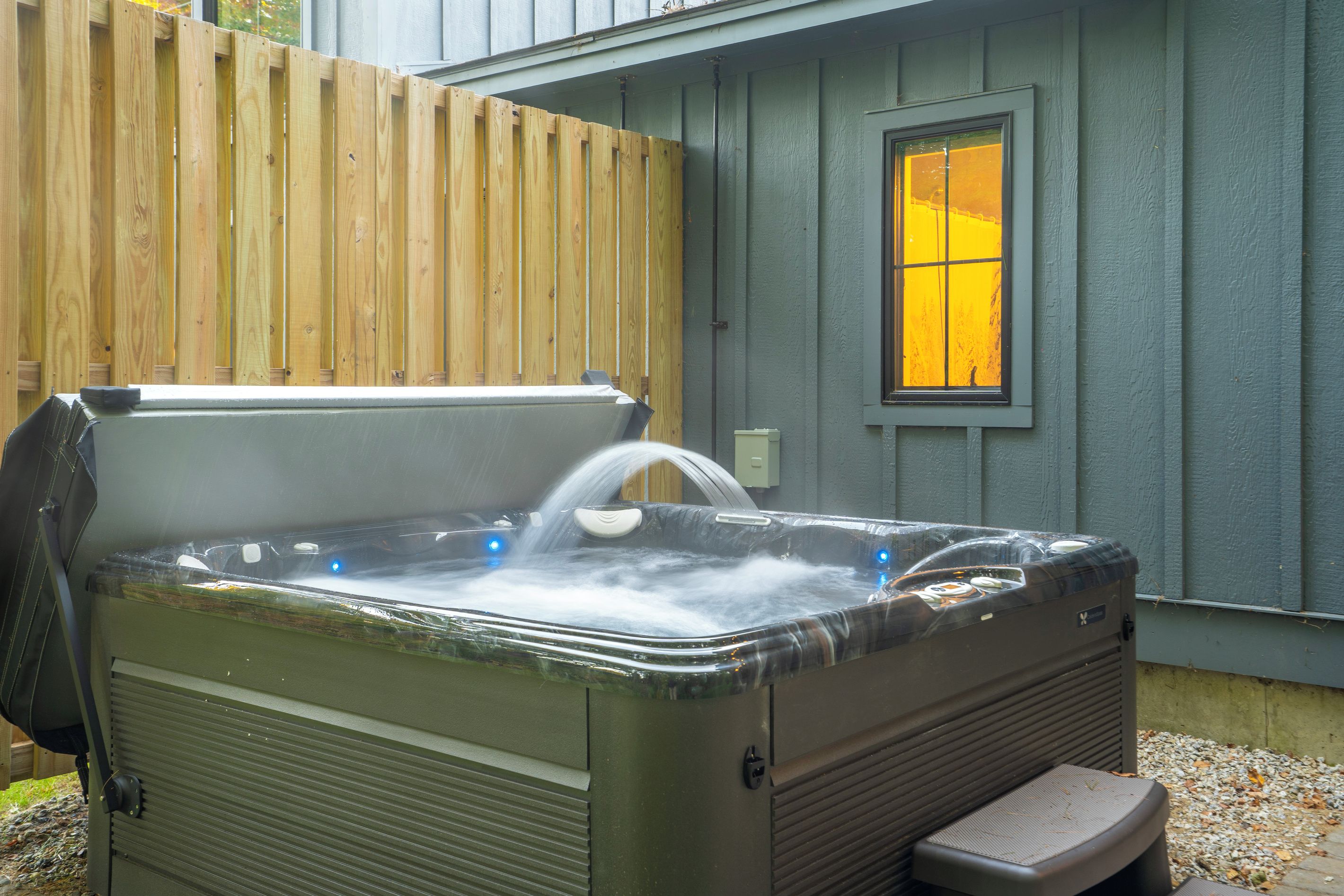 A hot tub with a wooden fence and a window in the background.