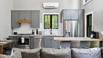 A modern kitchen with grey cabinets, a stainless steel refrigerator, and a window with a view of trees.